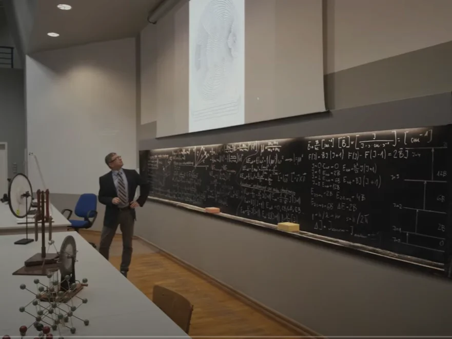 Tablica na auli Fizyki pokryta wzorami, wykładowca w czasie prezentacji multimedialnej.